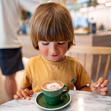 Zufriedenes Kind mit einer Tasse Kakao an einem der Tische im Familiencafé.